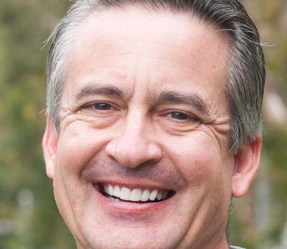 MIddle aged man standing in front of a tree and smiling