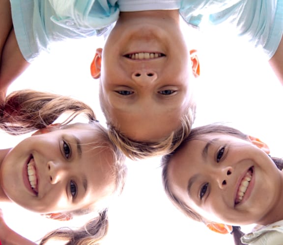 Three kids with arms around each other looking down at the camera and smiling
