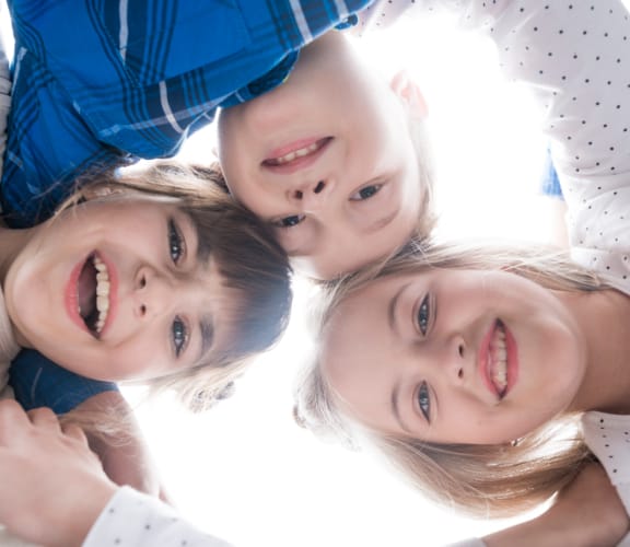 Three kids with arms around each other looking down at the camera and smiling